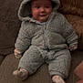 baby, child, onesie, blue_clothing, couch, pillow, soft_texture, indoor, cute, smiling, seated, hood, face, person, cozy, infant, warm_clothing, sock, plush, home