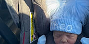 Theo is registered to the contest to win money with this photo: newborn, baby, car_seat, hat, blue, blanket, infant, sleeping, pom_poms, clothing, child, person, seatbelt, interior, car, sunlight, shadow, cozy, cute, bundle