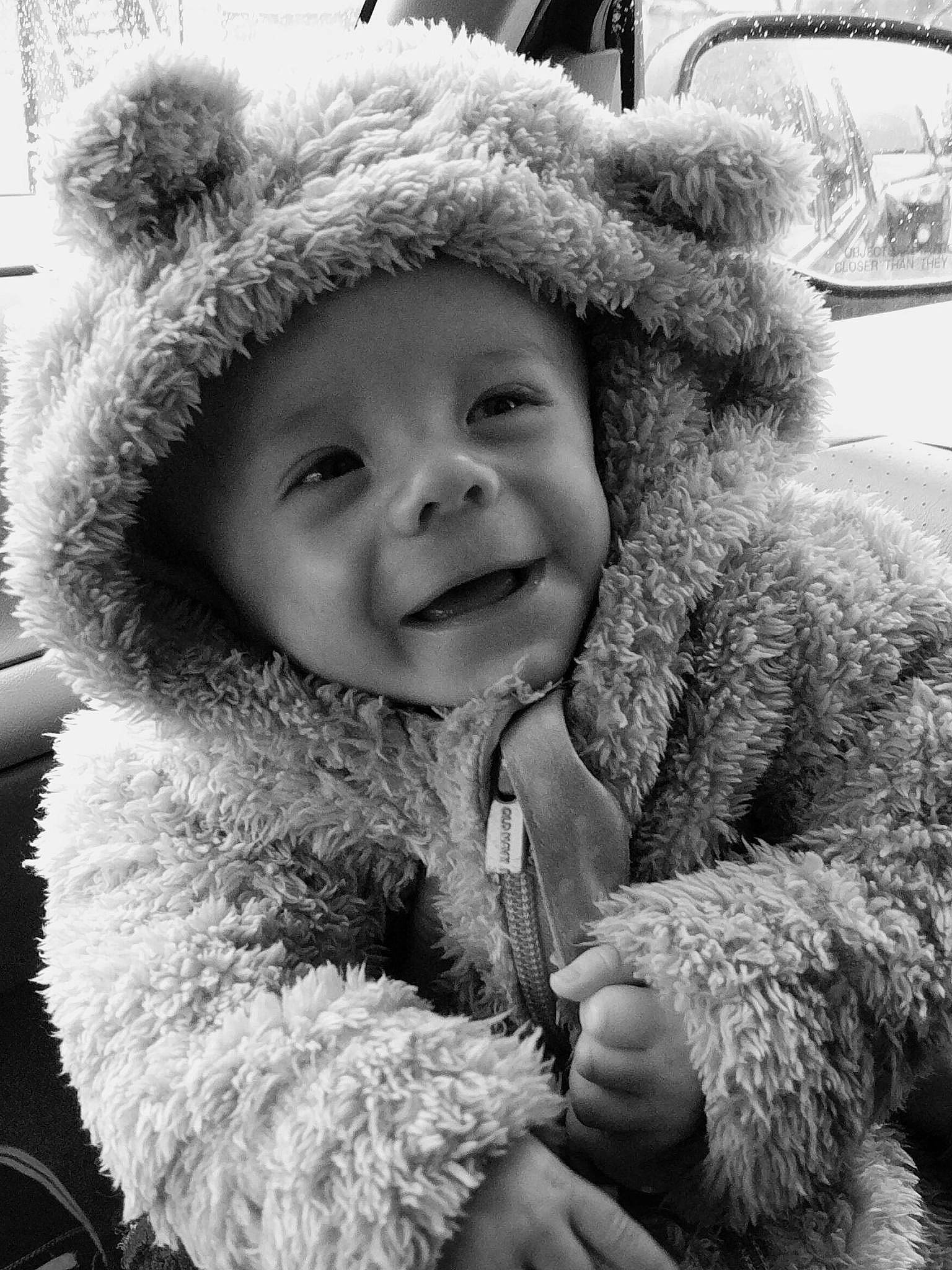 Malachi is registered to the contest to win money with this photo: black_and_white, eye, facial_expression, fur_clothing, gesture, hand, happy, headgear, headwear, mammal, nose, outerwear, person, photograph, skin, smile, standing, style, textile, toddler