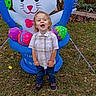 child, decoration, easter_bunny, easter_eggs, festive, flowers, garden, grass, holiday, inflatable, jeans, leaves, outdoor, person, plaid_shirt, playful, shoes, smiling, spring, toddler
