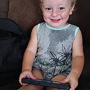 Huxon is registered to the contest to win money with this photo: toddler, child, smiling, sitting, couch, brown_couch, handheld_device, gaming, socks, casual_clothing, indoor, happy, light_hair, eyes, person, young_child, furniture, relaxed, playful, portrait