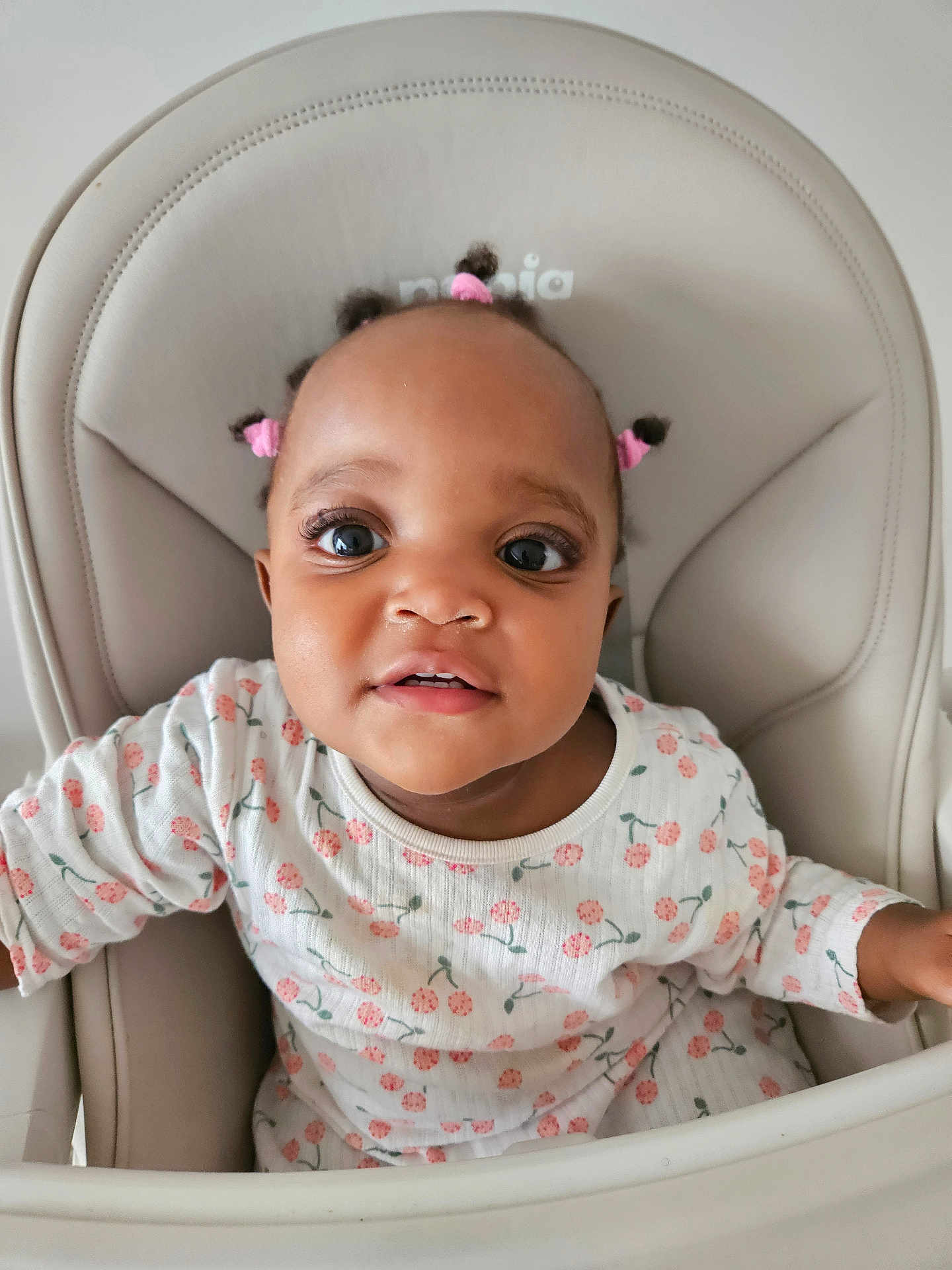 Abby a rejoint le concours — aidez-le/la à gagner de superbes lots ! baby, child, high_chair, pink_hair_ties, white_outfit, floral_pattern, indoor, cute, portrait, face, smiling, seated, infant, curious, closeup, skin, cute_expression, young_child, person, furniture