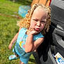 Nyomi joined the competition — help win amazing prizes! child, girl, curly_hair, blue_clothing, outdoor, grass, car, door, pouting, playful, sunny, daylight, blurry_background, standing, person, cute, summer, expression, portrait, leisure