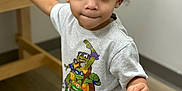 Hysean joined the competition — help win amazing prizes! toddler, child, curly_hair, indoor, table, tshirt, teenage_mutant_ninja_turtles, shorts, floor, wooden_table, brown_eyes, person, young_child, casual_clothing, standing, looking_up, lip_bite, cute, curious, light_background