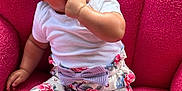 Dahlilah is registered to the contest to win money with this photo: baby, child, headband, bow, white_shirt, floral_pants, sitting, pink_chair, hand_in_mouth, cute, infant, portrait, comfortable, indoor, colorful, happy, soft_texture, footwear, person, smiling