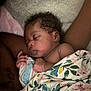 baby, sleeping, blanket, floral_pattern, curly_hair, skin, arm, hand, comfort, soft_texture, peaceful, rest, infant, closeup, portrait, indoor, cuddle, relaxation, cozy, child