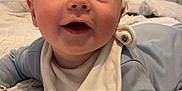 Hunter is registered to the contest to win money with this photo: baby, infant, bed, blanket, blue_clothing, bib, face, happy, head, indoor, infant_clothing, laying_down, mouth_open, person, portrait, smile, soft_texture, white_blanket, young_child, cute