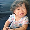 toddler, child, curly_hair, smiling, happy, car, car_interior, seat, keychain, barcode, floral_dress, cute, portrait, baby, hands, window, sunlight, seatbelt, person, indoors