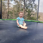 Annabelle is registered to the contest to win money with this photo: baby, blue_clothing, child, daylight, fun, grass, happy, joy, nature, outdoor, play, recreation, sitting, smiling, summer, sunlight, toddler, trampoline, trees, young_child