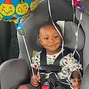 Kingsley is registered to the contest to win money with this photo: toddler, child, car_seat, birthday_balloons, smiling, harness, dinosaur_shirt, seatbelt, car_interior, celebration, party, colorful, happy, infant, young_child, sitting, vehicle, strapped_in, cute, ribbons