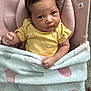 baby, infant, blanket, heart_pattern, yellow_clothing, pink_cushion, face, person, indoor, car_seat, soft_texture, cute, newborn, wrapped, child, expression, looking_up, cozy, comfort, small_hand