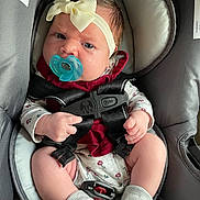 Amirah is registered to the contest to win money with this photo: baby, pacifier, car_seat, headband, infant, clothing, sock, straps, sitting, child, cute, face, hands, legs, indoor, expression, person, closeup, pink, gray