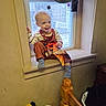 bedpost, casual_clothing, child, curtain, daylight, furniture, happy, indoor, light, overalls, person, plush_toys, room, sitting, smile, socks, toddler, wall, window, wood