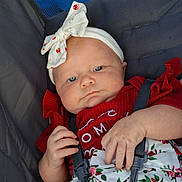 Sophia is registered to the contest to win money with this photo: baby, infant, child, stroller, portrait, face, blue_eyes, headband, bow, red_clothing, floral_pattern, sitting, harness, seatbelt, indoor, closeup, serious_expression, hands, fabric, photography