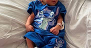 Liam is registered to the contest to win money with this photo: newborn, baby, sleeping, hospital_bed, blue_outfit, hat, socks, stitch_character, infant, bed, blanket, medical_wristband, cute, peaceful, indoors, child, person, resting, soft_lighting, pillow