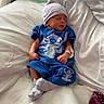 newborn, baby, sleeping, hospital_bed, blue_outfit, hat, socks, stitch_character, infant, bed, blanket, medical_wristband, cute, peaceful, indoors, child, person, resting, soft_lighting, pillow
