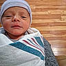Liam joined the competition — help win amazing prizes! newborn, baby, infant, wrapped, blanket, hat, striped_hat, face, person, indoors, wooden_floor, closeup, portrait, cute, human, child, sleepy, small, skin, cozy