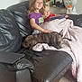 Lola is registered to the contest to win money with this photo: child, children, dog, couch, blanket, tablet, living_room, fan, carpet, leather, brindle, smiling, sitting, relaxed, indoor, family, cozy, home, furniture, casual