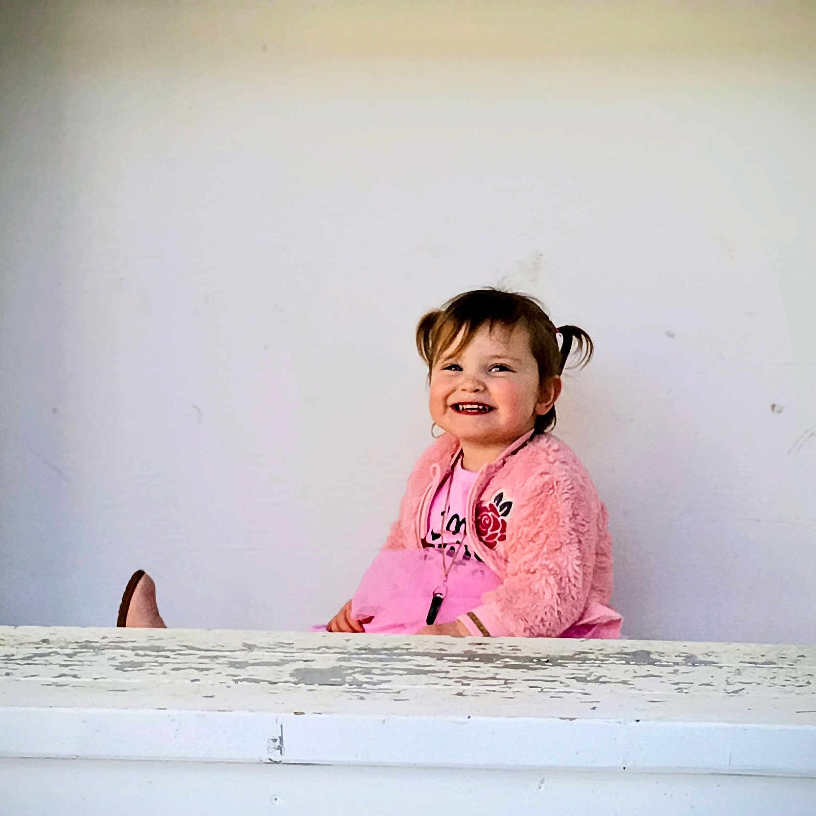 Sigrún joined the competition — help win amazing prizes! casual_clothing, child, cute, expression, face, girl, happy, indoor, jewelry, joy, person, pigtails, pink_jacket, portrait, sitting, smiling, toddler, weathered_surface, white_background, young_child