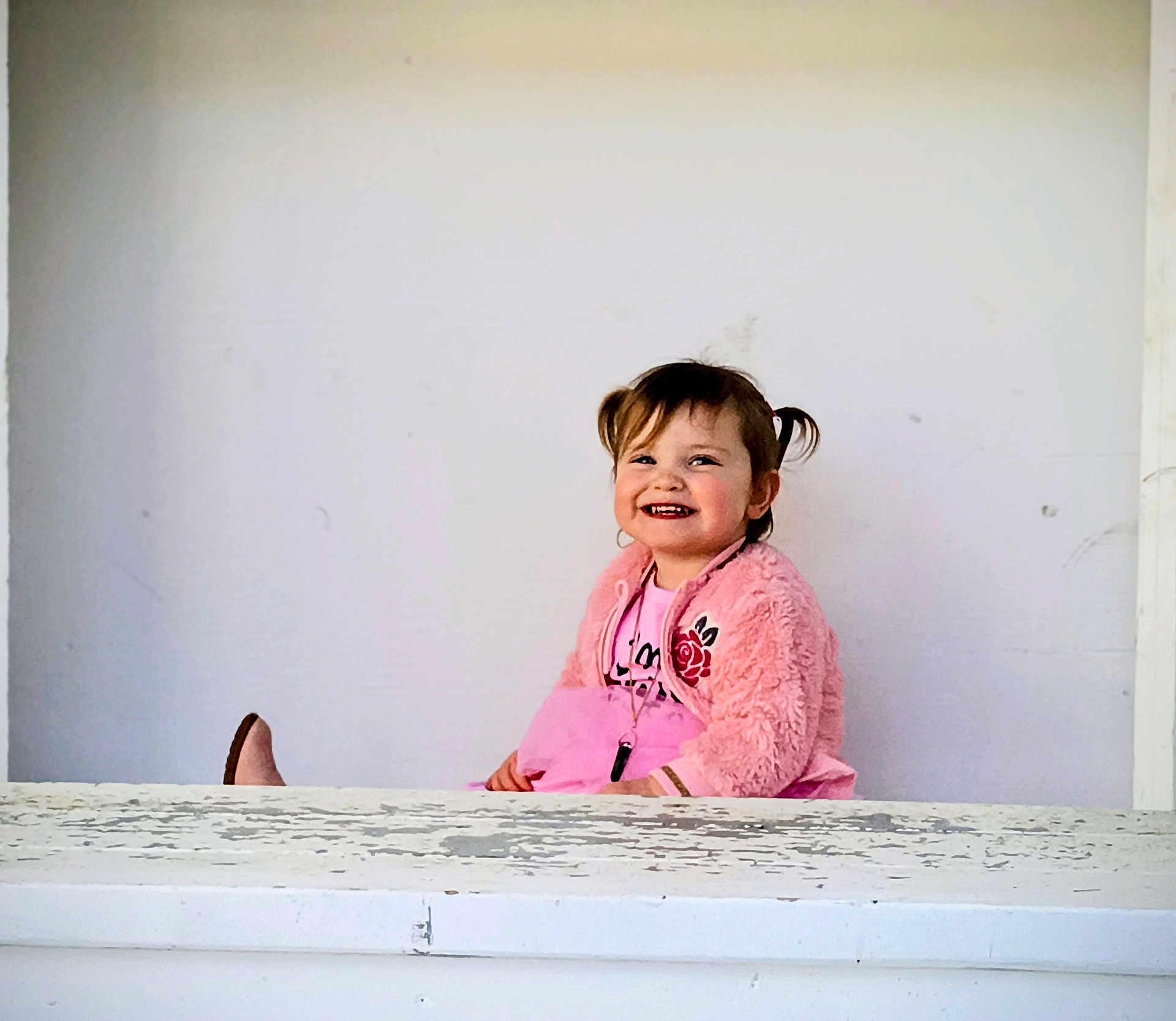 Sigrún joined the competition — help win amazing prizes! casual_clothing, child, cute, expression, face, girl, happy, indoor, jewelry, joy, person, pigtails, pink_jacket, portrait, sitting, smiling, toddler, weathered_surface, white_background, young_child