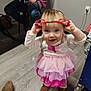 Sigrún is registered to the contest to win money with this photo: adult, boots, child, clothing, dress, face, floor, hair, headband, heart_shaped, indoor, person, pink, playful, sitting, smiling, table, toddler, toy, wooden_floor