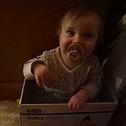 Sigrún joined the competition — help win amazing prizes! baby, baby_wipes, box, cardboard_box, child, clothing, curious, cute, dim_lighting, face, floor, hand, home, indoor, infant, looking_up, pacifier, person, sitting, young_child