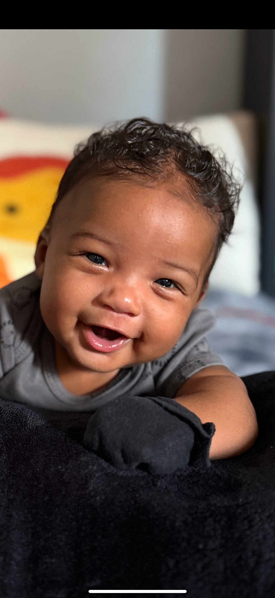 Benjamin is registered to the contest to win money with this photo: baby, smile, face, child, curly_hair, black_mitten, grey_clothing, blanket, indoor, portrait, cute, happy, infant, closeup, soft_texture, warm_lighting, background_blur, person, toddler, expression