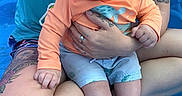 Castiel joined the competition — help win amazing prizes! adult, baby, blue_pool, child, cute, hand, happy, holding, legs, orange_shirt, outdoor, person, play, shorts, sitting, skin, smiling, summer, tattoo, water