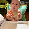 baby, child, toy, teddy_bear, high_chair, curious, indoor, person, face, expression, seat, furniture, clothing, striped_shirt, hand, head, skin, eyes, mouth, infant