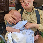 Castiel is registered to the contest to win money with this photo: child, baby, blanket, outdoor, smiling, face, person, sitting, clothing, suspenders, infant, holding, happy, portrait, grass, brick_wall, chair, cute, family, toddler