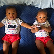 Dayton is registered to the contest to win money with this photo: baby, infant, twin, matching_clothes, red_shorts, blue_cushion, holding_hands, cute, indoor, portrait, child, smiling, socks, short_sleeve, lying_down, two_children, people, young, happy, casual