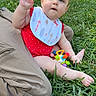 Aurora is registered to the contest to win money with this photo: baby, bib, casual, child, cute, daytime, grass, greenery, infant, legs, nature, outdoor, park, person, playing, polka_dot, red_clothing, sitting, sunlight, toy