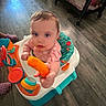 baby, blue_eyes, cheesy_puff, child, colorful, crib, curious, flooring, food, furniture, home, indoor, infant, person, pink_clothing, playtime, snack, toy, walker, young_child