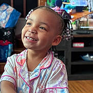 Airiye joined the competition — help win amazing prizes! child, smiling, pajamas, indoors, beads, braids, happy, face, person, cute, living_room, wood_floor, television, furniture, colorful, portrait, toddler, young_child, joy, casual_clothing