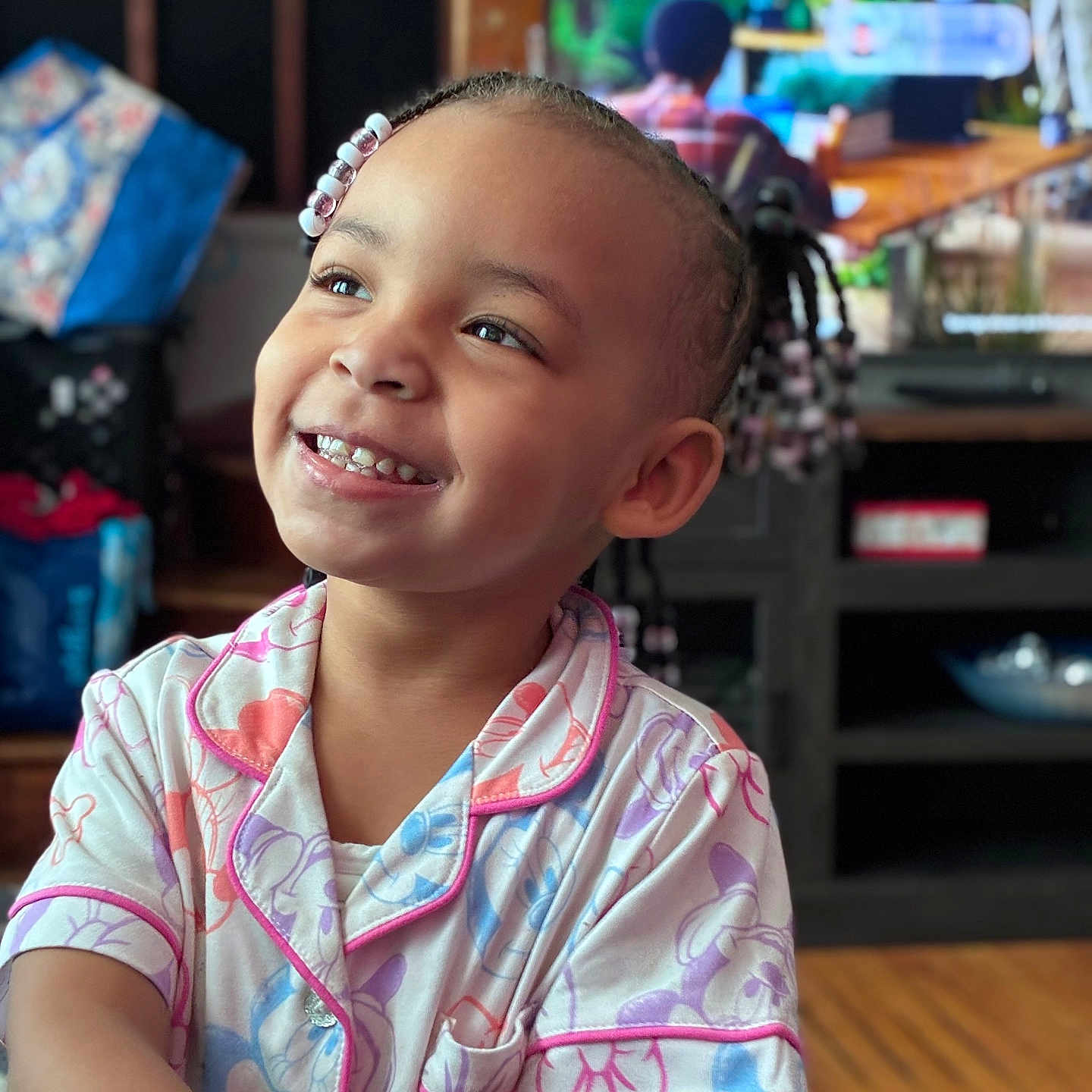 Airiye joined the competition — help win amazing prizes! child, smiling, pajamas, indoors, beads, braids, happy, face, person, cute, living_room, wood_floor, television, furniture, colorful, portrait, toddler, young_child, joy, casual_clothing