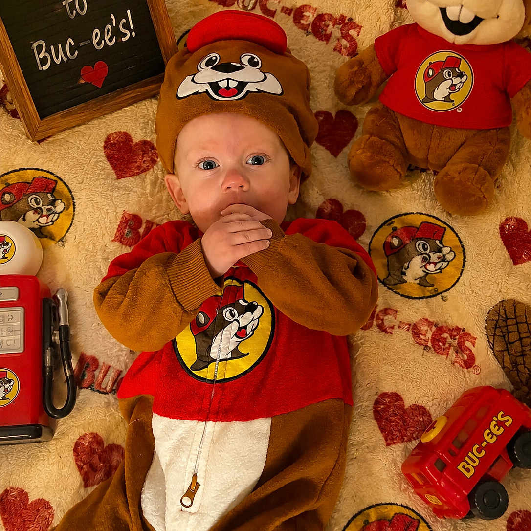 Hunter joined the competition — help win amazing prizes! baby, infant, child, portrait, lying_down, smiling, wide_eyed, costume, beaver_costume, red_shirt, plush_toy, stuffed_animal, blanket, heart_pattern, toy_truck, welcome_sign, indoor, themed_setup, buc_ee's, cozy