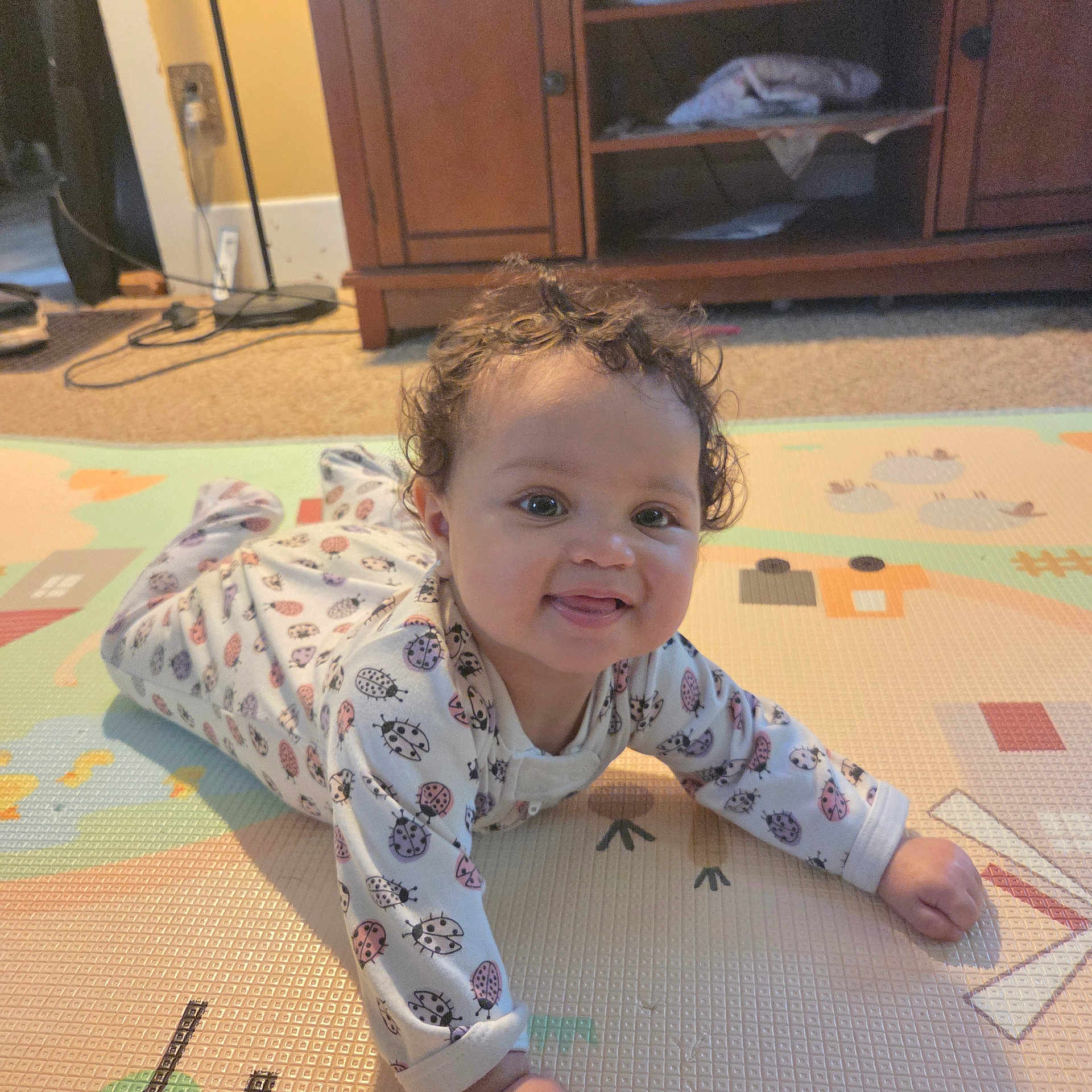 Wynterlynn Bonds joined the competition — help win amazing prizes! baby, cabinet, carpet, child, crawling, curly_hair, cute, face, floor, happy, home, indoor, infant, onesie, patterned_clothing, person, play_mat, smile, tongue_out, wooden_furniture
