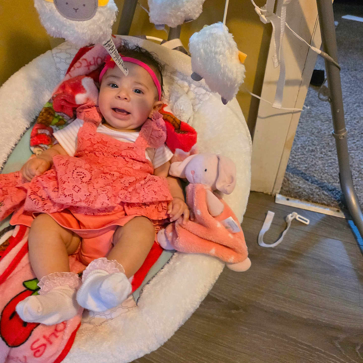 Yaretzy is registered to the contest to win money with this photo: baby, infant, baby_swing, plush_toy, stuffed_animal, headband, pink_clothing, white_socks, flooring, wood_floor, baby_blanket, toy_sheep, indoor, child, happy, cute, seated, soft_toys, home, playtime