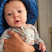 Aaliyah joined the competition — help win amazing prizes! baby, child, hand, hat, blue_eyes, floral_clothing, onesie, indoor, door, chain_lock, person, face, curious, expression, skin, adult_hand, holding, portrait, closeup, headwear