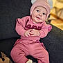 baby, child, pink_clothing, knitwear, hat, ears, drool, couch, indoor, cozy, cute, sitting, portrait, infant, warm_clothing, footwear, happy, smiling, face, hands