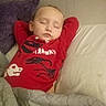 child, sleeping, bed, pillow, blanket, quilt, red_shirt, dinosaur, indoors, cozy, resting, peaceful, young, toddler, portrait, person, clothing, head, face, relaxation