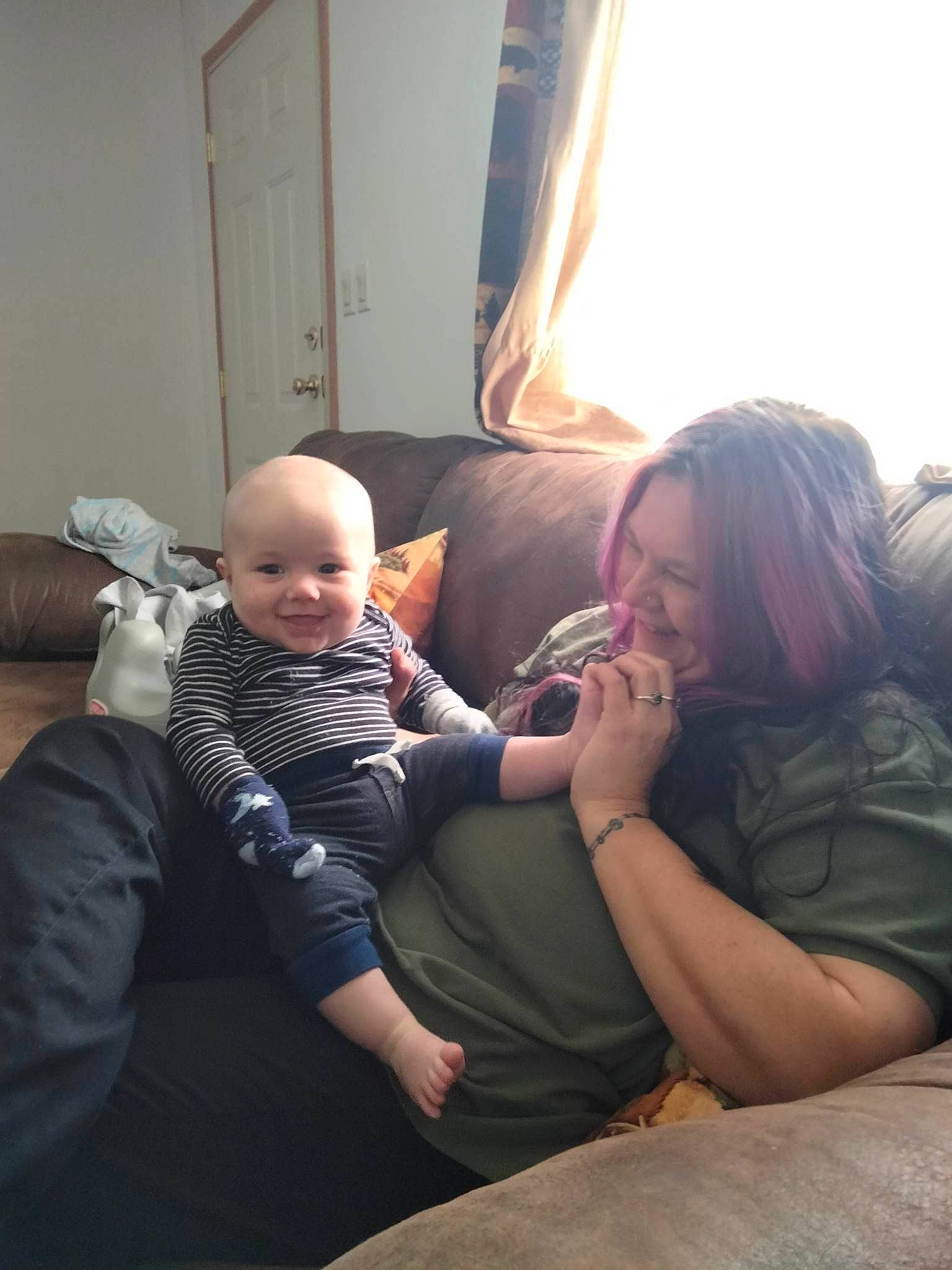 Jason is registered to the contest to win money with this photo: baby, comfort, couch, curtain, door, event, finger, fun, happy, human_leg, joy, lap, living_room, person, sitting, skin, smile, thigh, toddler, tree