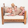 baby, child, cozy, cushion, cute, hat, infant, knitted_clothing, looking_at_camera, lying_down, neutral_background, pillow, pom_pom, portrait, relaxed, skin, small_bed, soft_lighting, studio, wooden_bed