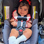 Skyler joined the competition — help win amazing prizes! baby, car_seat, child, clothing, cute, fabric, face, furniture, happy, head_accessory, indoor, infant, person, portrait, red_bow, seatbelt, sitting, smiling, white_socks, young_child