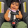 baby, car_seat, smiling, child, purple_bow, green_pants, white_top, pink_shoes, nike, plush_toys, safety_harness, infant, cute, happy, indoor, portrait, seatbelt, child_seat, black_hair, playful