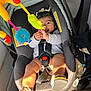baby, car_seat, child, infant, toy, colorful_toys, smiling, happy, seatbelt, footwear, sandal, sunlight, indoor, person, cute, clothing, seat, car_interior, play, hands