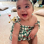 Louella joined the competition — help win amazing prizes! baby, child, smiling, sitting, dress, headband, indoor, floor, hand, person, happy, cute, playtime, infant, young_child, patterned_clothing, holding_hand, pillow, toy, background