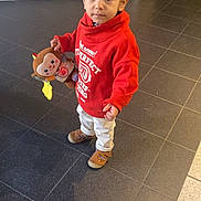 Ilyan a rejoint le concours — aidez-le/la à gagner de superbes lots ! toddler, child, indoor, toy, stuffed_animal, curly_hair, red_sweatshirt, white_pants, brown_shoes, floor_tiles, person, young_child, looking_at_camera, cute, casual_clothing, playful, expression, standing, holding_toy, curious