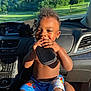 Kaysyn is registered to the contest to win money with this photo: toddler, child, smiling, happy, indoor, car, dashboard, shorts, holding_object, sunlight, greenery, window, person, hand, seat, seatbelt, blue_shorts, black_pouch, skin, curly_hair
