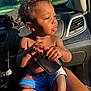 Kaysyn is registered to the contest to win money with this photo: toddler, child, car_interior, sunlight, black_pouch, shorts, person, hand, lap, window, seat, dashboard, vent, skin, curly_hair, outdoor_view, nature, greenery, daylight, portrait